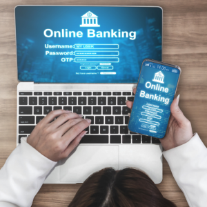 Pessoa digitando em um laptop com interface de Online Banking e segurando um smartphone que exibe o logo de banco online, representando transações e pagamentos.