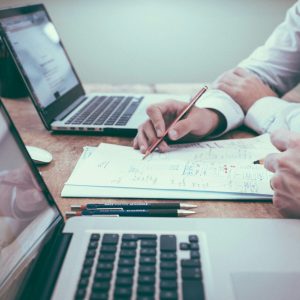Duas pessoas analisando documentos financeiros com anotações e gráficos, com laptops em primeiro plano, representando o controle de reembolsos e prevenção de prejuízos.